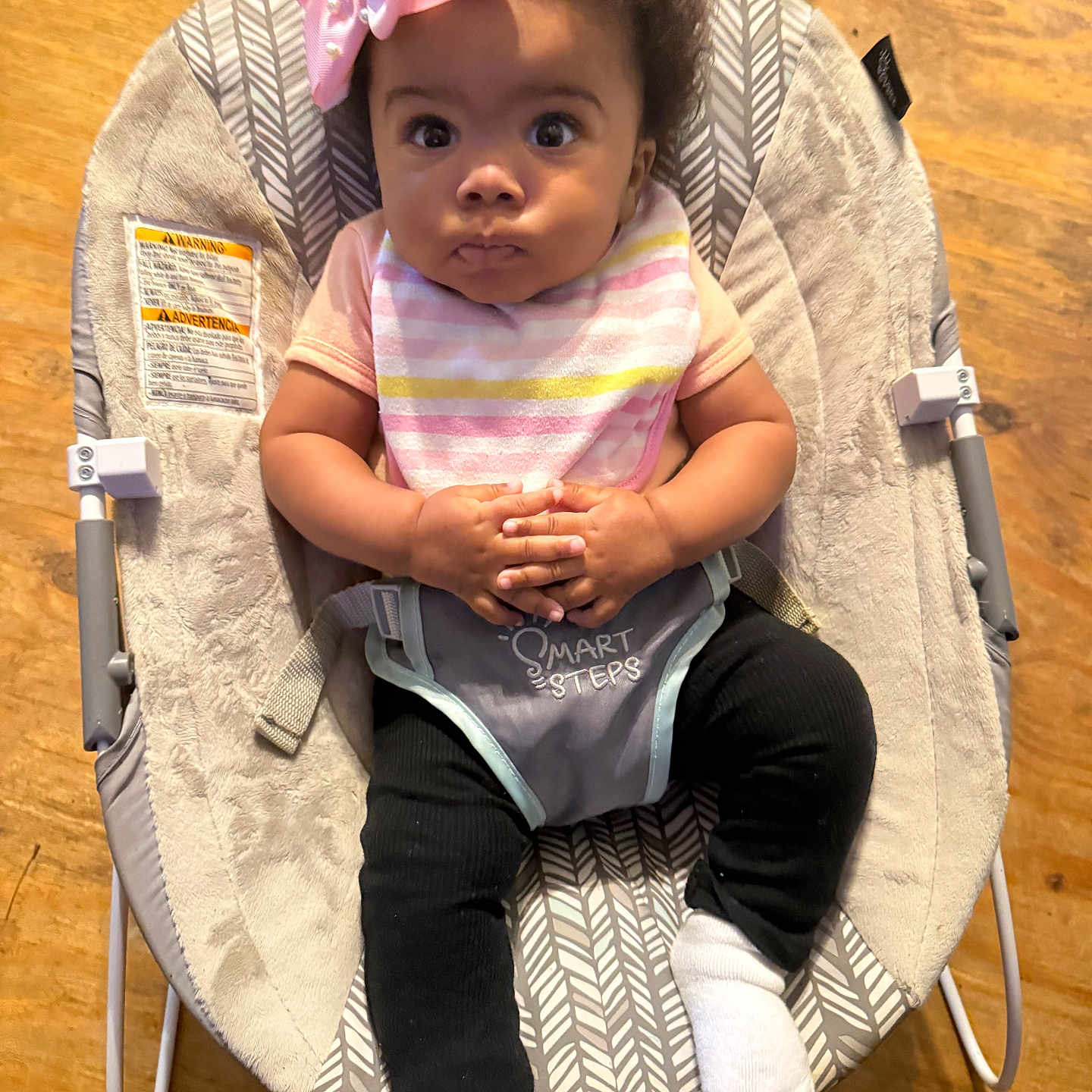 Icelynn joined the competition — help win amazing prizes! baby, baby_clothing, baby_rocker, bib, black_pants, child, comfort, cute, hands_clasped, indoor, infant, pink_bow, portrait, seat, serious_expression, small_hands, white_socks, wide_eyes, wooden_floor, young_child