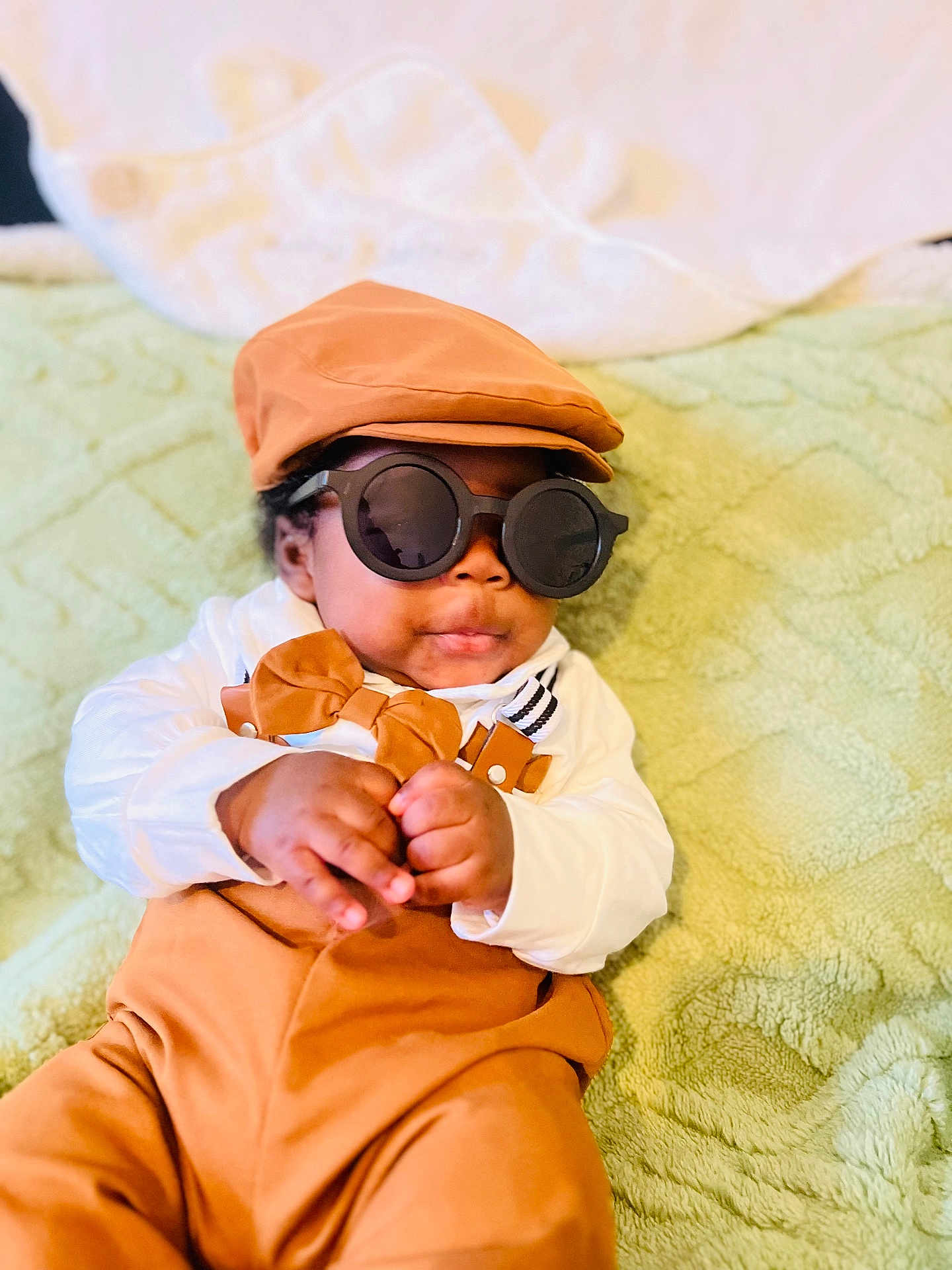 Stetson joined the competition — help win amazing prizes! baby, child, sunglasses, hat, bow_tie, suspenders, clothing, green_blanket, infant, cute, portrait, fashion, accessory, indoor, soft_texture, hands, face, smile, relaxed, person
