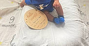 Amari joined the competition — help win amazing prizes! baby, blue_clothing, child, curly_hair, cute, floor, flooring, home, indoor, infant, looking_up, milestone, milestone_blanket, person, portrait, sitting, socks, vent, wooden_plaque, wooden_ring