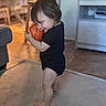 Mykenzie is registered to the contest to win money with this photo: toddler, child, basketball, black_onesie, barefoot, smile, indoor, living_room, carpet, furniture, table, chair, television, wood_floor, toy, cute, happy, person, home, play