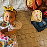 Mykenzie joined the competition — help win amazing prizes! baby, child, infant, headband, yellow_bow, embroidered_dress, colorful, smiling, holding_object, 8_months_card, bread, traditional_bread, cup, coffee_jar, tablecloth, fabric, lying_down, portrait, indoors, cute