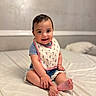 baby, child, smiling, sitting, bed, bib, denim_shorts, cute, happy, indoor, person, infant, portrait, skin, foot, hand, clothing, young, face, cozy