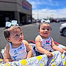 baby, blue_sky, blurred_background, bow, car, child, cute, daylight, happy, outdoor, parking_lot, patterned_clothing, shopping_cart, store, stroller, summer, sunny, toddler, two_children, white_tank_top