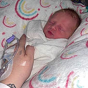 Lily is registered to the contest to win money with this photo: newborn, baby, blanket, swaddled, sleeping, hand, hospital, iv_line, wristband, tattoo, pillow, rainbow_pattern, skin, person, medical, resting, infant, cute, comfort, tender