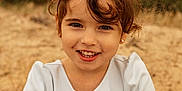 Capucine participe au concours pour gagner de l'argent avec cette photo : bangs, beach, brown_hair, candy, child, close_up, dress, earrings, eyes, girl, hands, happy, nature, outdoor, portrait, sand, sitting, smiling, snack, toddler