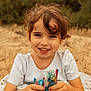 bangs, beach, brown_hair, candy, child, close_up, dress, earrings, eyes, girl, hands, happy, nature, outdoor, portrait, sand, sitting, smiling, snack, toddler