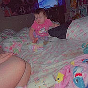 Theresa is registered to the contest to win money with this photo: baby, pajamas, blanket, bed, floral, toy, television, room, birthday_banner, party, child, person, indoor, furniture, colorful, pink, purple, decorations, sleepwear, cushion