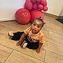 toddler, child, face_paint, balloons, pink_balloons, wooden_floor, curious, indoor, casual_clothing, slippers, sitting, looking_up, decorations, young_child, floor_tiles, cute, portrait, person, playful, happy