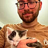 Hakira participe au concours pour gagner de l'argent avec cette photo : man, glasses, beard, kitten, cat, sleeping, holding, brown_shirt, hand, indoor, portrait, smiling, close_up, cute, pet, young_adult, gentle, affection, casual, warm_lighting