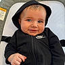 baby, infant, hoodie, black_clothing, nike_logo, smile, blue_eyes, face, hand, seated, indoors, portrait, cute, child, young, cozy, fabric, texture, clothing, person