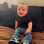 Jason is registered to the contest to win money with this photo: baby, child, smiling, sitting, blue_eyes, black_shirt, jeans, sneakers, bed, pillow, indoor, wooden_wall, cute, happy, portrait, young_child, clothing, footwear, infant, casual