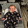 baby, pacifier, onesie, pittsburgh_steelers, baby_seat, cushion, indoor, dining_chair, table, flooring, infant, clothing, person, child, face, hand, footwear, wood_floor, black_bag, home_interior