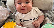 Jason is registered to the contest to win money with this photo: baby, champion_logo, child, cushion, cute, expression, face, furniture, happy, high_chair, home, indoor, infant, person, portrait, seat, smile, towel, toy, white_shirt