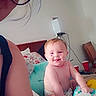 baby, diaper, smile, person, adult, glasses, bed, pillow, wipes, room, chair, cup, wall, device, hair, face, skin, indoor, furniture, candid