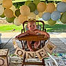 baby, high_chair, birthday, balloons, banner, winnie_the_pooh, party, outdoor, child, celebration, wooden_chair, decorations, tablecloth, grass, sunlight, cute, one_year_old, event, childrens_party, infant