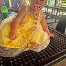 toddler, child, yellow_dress, pacifier, picnic_table, park, playground, bottle, person, outdoor, pavilion, summer, daylight, clothing, sitting, baby, expression, face, hand, foot