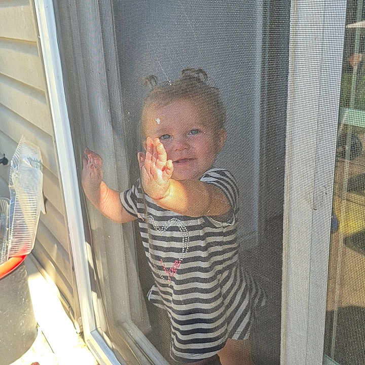 Renezmae is registered to the contest to win money with this photo: toddler, child, striped_dress, glass_door, screen, smiling, sunlight, shadow, outdoor, curious, happy, barefoot, door_frame, person, young_child, baby, playful, candid, home, daylight