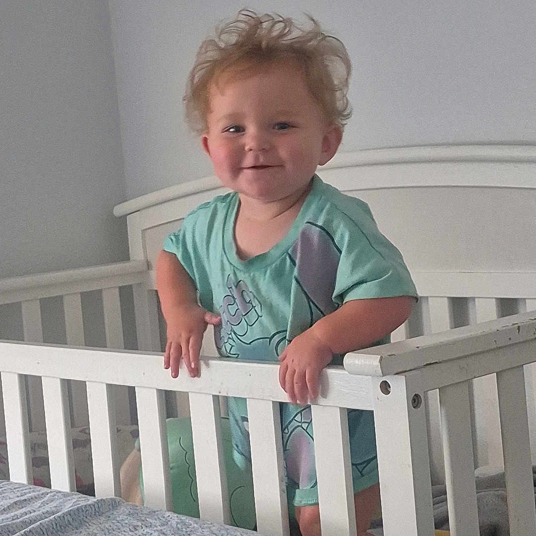 Renezmae joined the competition — help win amazing prizes! toddler, child, crib, bedroom, white_crib, smiling, blonde_hair, tousled_hair, standing, gripping, railing, indoor, bed, blanket, plush_toy, light_wall, casual_clothing, cute, happy, infant