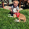 child, toddler, dog, grass, outdoor, sunny, pet, harness, red, green, table, adult, backyard, casual, person, smile, summer, grass_lawn, barefoot, relax