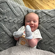 Dakota is registered to the contest to win money with this photo: baby, blanket, mittens, couch, floor, wood_floor, smile, infant, face, clothing, texture, cozy, indoor, person, happy, head, seated, home, soft, young_child