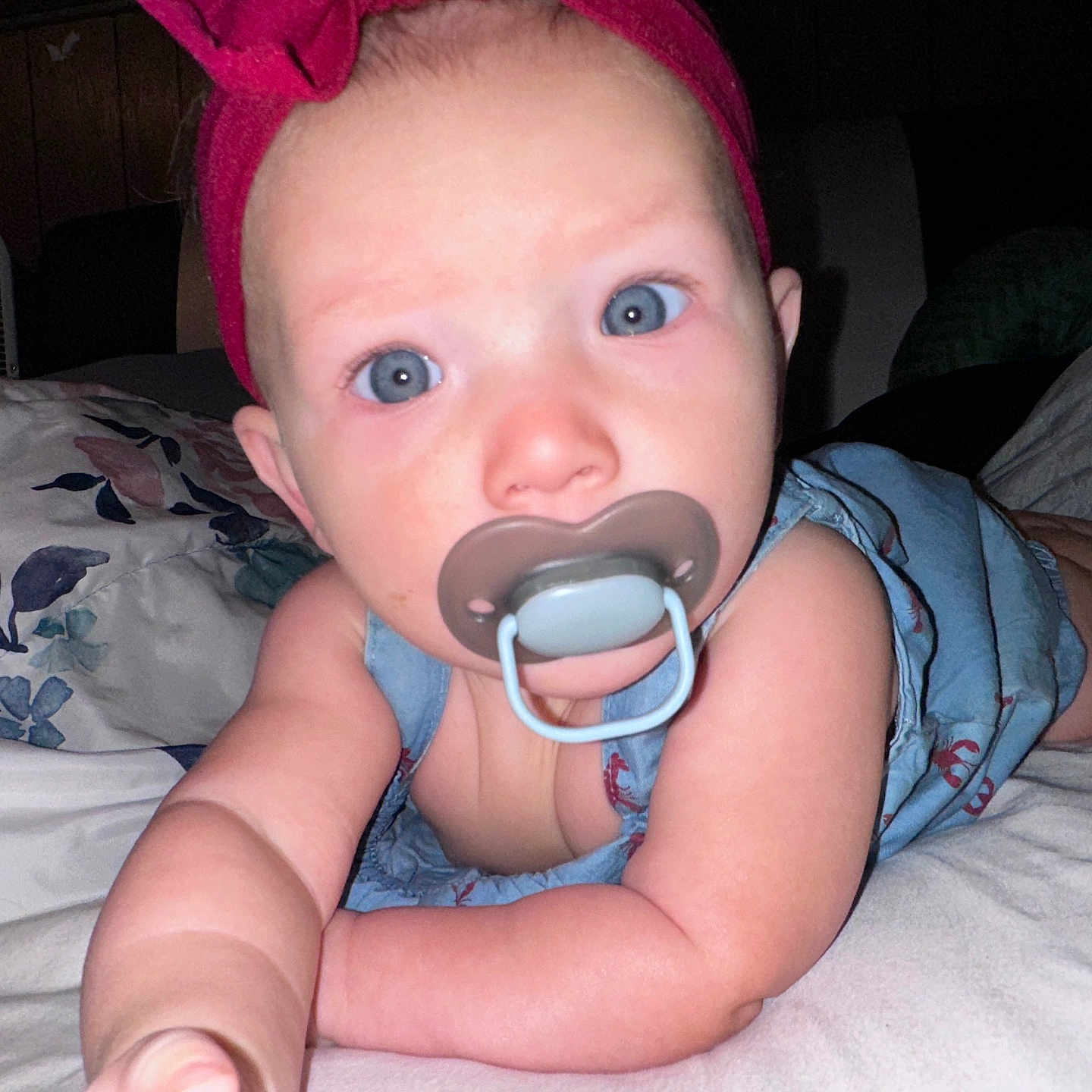 Melinna Mae is registered to the contest to win money with this photo: baby, pacifier, headband, blue_eyes, infant, bed, arm, skin, clothing, indoor, person, cute, young_child, portrait, child, face, expression, reaching, laying, closeup