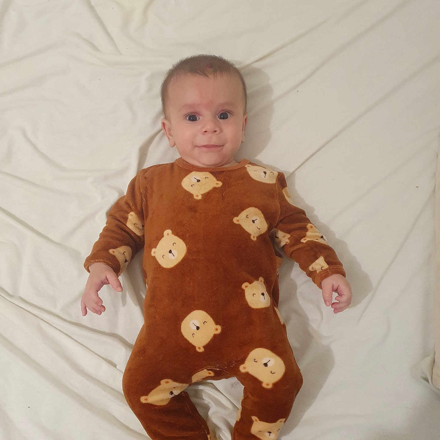 Eiden a rejoint le concours — aidez-le/la à gagner de superbes lots ! baby, infant, onesie, brown_clothing, bear_pattern, lying_down, white_sheet, cute, child, portrait, indoors, sleepwear, footed_pajamas, smiling, face, person, young_child, cozy, comfortable, sleeping_area
