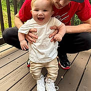 Mylo joined the competition — help win amazing prizes! baby, child, person, sneakers, white_shirt, beige_pants, cap, outdoor, deck, wooden_floor, greenery, happy, smiling, crouching, hands, casual_clothing, nature, daylight, supporting, portrait