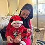 baby, woman, holiday_clothing, santa_hat, red_outfit, smile, indoor, couch, lamp, window, decor, floor, rug, person, home, cozy, festive, child, holding, joy