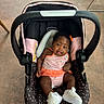 adorable, baby, baby_gear, car_seat, child, concrete_floor, curly_hair, indoors, infant, looking_at_camera, orange_bow, pink_clothing, portrait, safe, sitting, smiling, striped_outfit, stroller, tongue_out, white_shoes