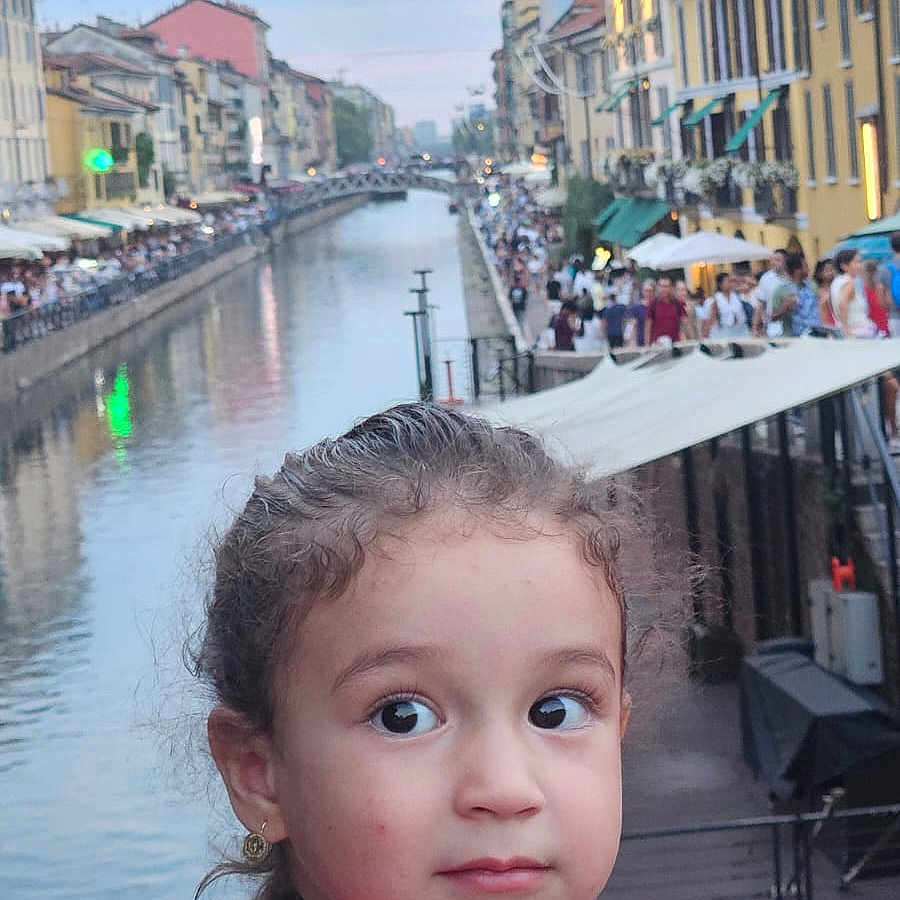 Isra participe au concours pour gagner de l'argent avec cette photo : buildings, canal, child, cityscape, crowd, curious, curly_hair, earrings, evening, girl, outdoor, people, pink_dress, portrait, side_view, tourist_spot, travel, urban, water, young