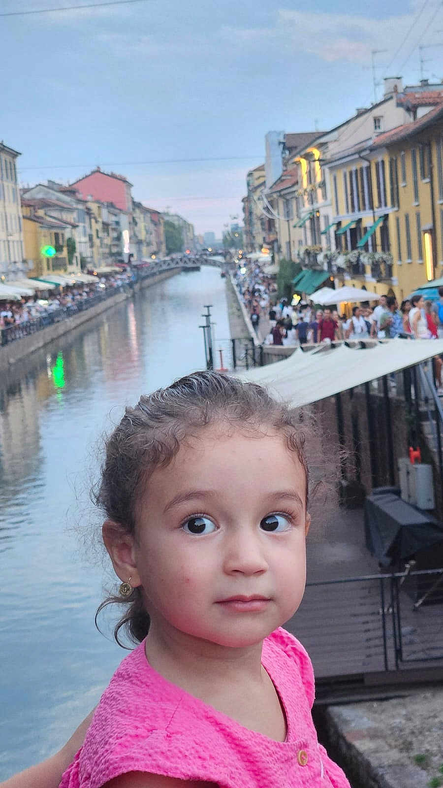 Isra participe au concours pour gagner de l'argent avec cette photo : child, girl, portrait, canal, water, cityscape, buildings, crowd, outdoor, evening, pink_dress, curly_hair, earrings, urban, travel, tourist_spot, people, side_view, young, curious