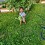 toddler, child, grass, watering_can, barefoot, smiling, garden, plants, greenery, outdoor, sunlight, rooster_statue, toy, yard, nature, happy, clothing, summer, playful, vegetation