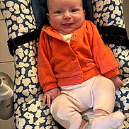 Romy a rejoint le concours — aidez-le/la à gagner de superbes lots ! baby, child, infant, smile, orange_jacket, white_pants, baby_seat, patterned_cushion, comfortable, cute, indoors, happy, person, sitting, soft_clothing, small_hands, footwear, playful, portrait, cozy