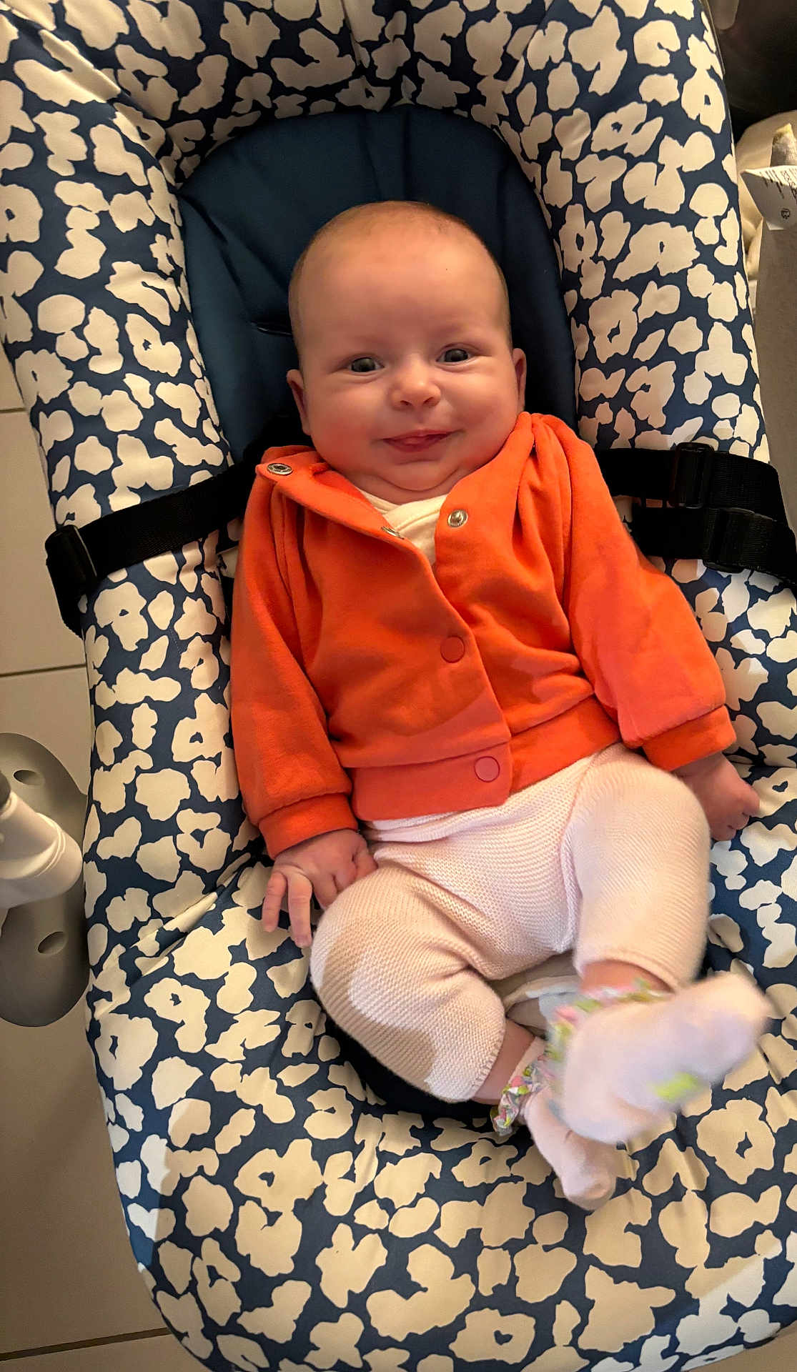 Romy a rejoint le concours — aidez-le/la à gagner de superbes lots ! baby, child, infant, smile, orange_jacket, white_pants, baby_seat, patterned_cushion, comfortable, cute, indoors, happy, person, sitting, soft_clothing, small_hands, footwear, playful, portrait, cozy