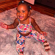 Riel joined the competition — help win amazing prizes! toddler, child, smiling, sitting, indoor, plush_rug, colorful_clothing, sandals, braided_hair, happy, cute, jewelry, necklace, earrings, wooden_floor, door, drawer, red_bracelet, person, portrait