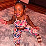 toddler, child, smiling, sitting, indoor, plush_rug, colorful_clothing, sandals, braided_hair, happy, cute, jewelry, necklace, earrings, wooden_floor, door, drawer, red_bracelet, person, portrait