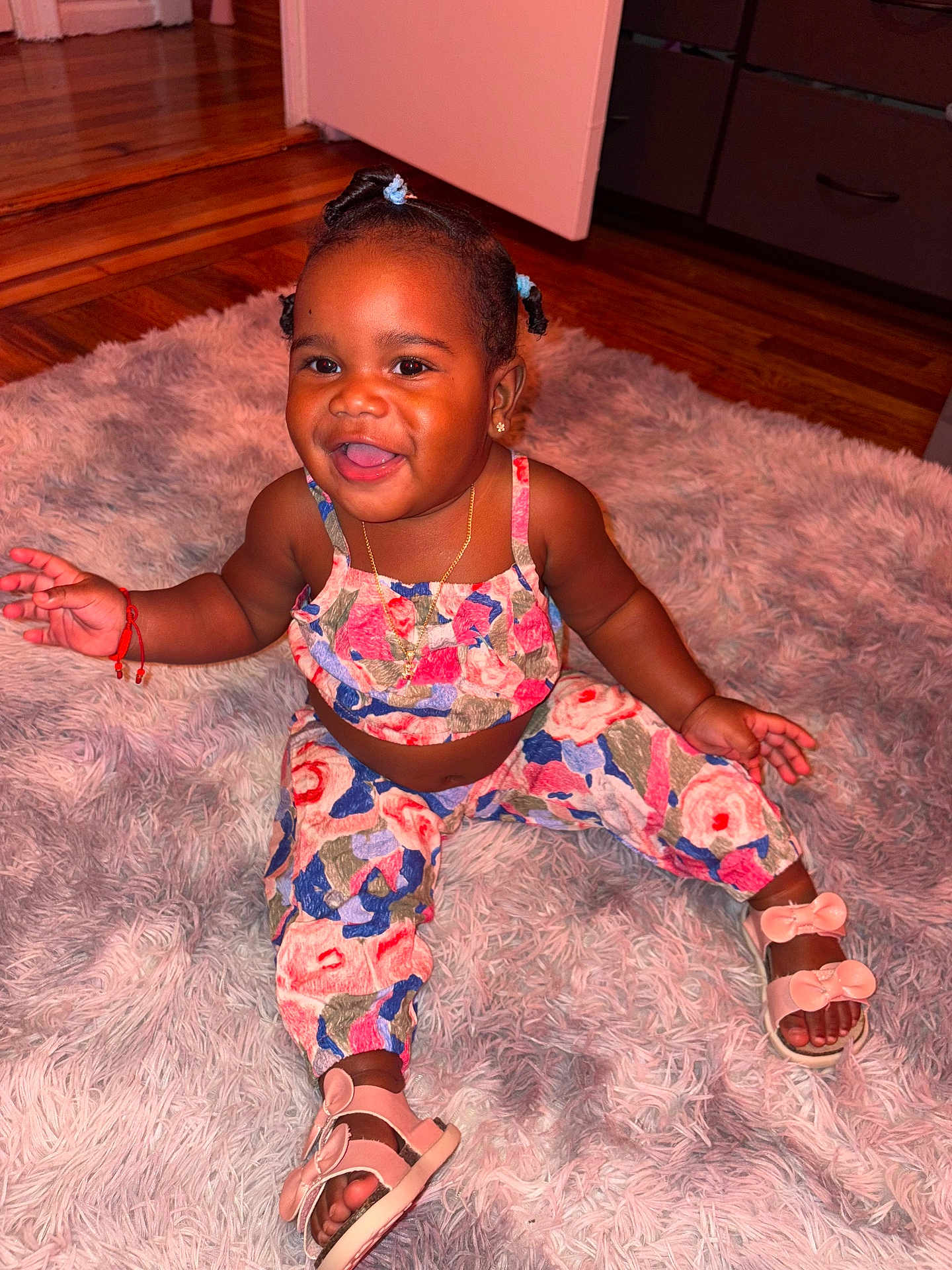 Riel joined the competition — help win amazing prizes! toddler, child, smiling, sitting, indoor, plush_rug, colorful_clothing, sandals, braided_hair, happy, cute, jewelry, necklace, earrings, wooden_floor, door, drawer, red_bracelet, person, portrait