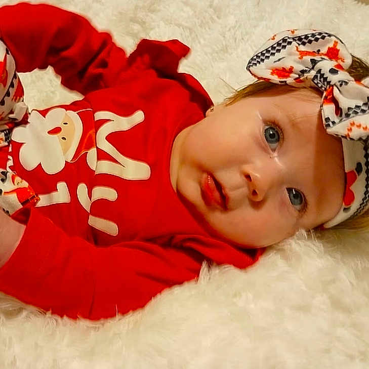 Azaria joined the competition — help win amazing prizes! adorable, baby, blue_eyes, bow, child, cute, expression, face, festive, fluffy_surface, headband, holiday_outfit, indoor, infant, lying_down, newborn, person, portrait, red_clothing, soft_texture