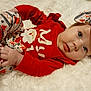 baby, infant, pajamas, red_clothing, white_background, headband, bow, face, blue_eyes, hand, lying_down, cute, holiday_theme, soft_texture, child, indoors, smile, cozy, portrait, person