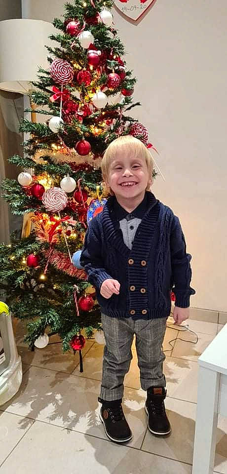 Aaron a rejoint le concours — aidez-le/la à gagner de superbes lots ! christmas, christmas_decoration, christmas_ornament, christmas_tree, clothing, conifer, event, evergreen, happy, holiday, holiday_ornament, jeans, joy, ornament, person, plant, sleeve, smile, standing, toddler