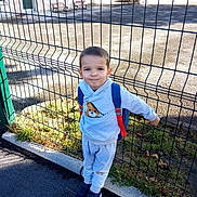 Logan a rejoint le concours — aidez-le/la à gagner de superbes lots ! child, boy, backpack, metal_fence, school_building, bench, pavement, grass, sneakers, hoodie, short_hair, smile, outdoors, playground_area, sidewalk, casual_clothing, portrait, daytime, street_curb, young_child