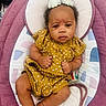 baby, infant, child, polka_dot, yellow_dress, flower_hair_accessory, pink_baby_seat, cushion, indoor, person, cute, portrait, skin, feet, hands, head, expression, relaxing, clothing, baby_seat