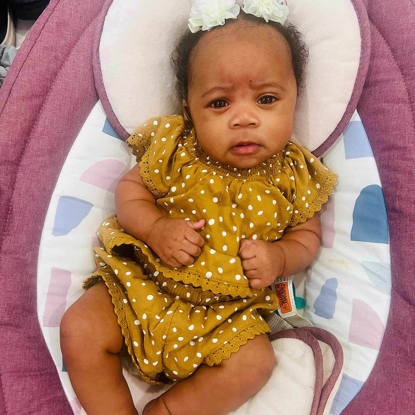 Sevyn is registered to the contest to win money with this photo: baby, infant, child, polka_dot, yellow_dress, flower_hair_accessory, pink_baby_seat, cushion, indoor, person, cute, portrait, skin, feet, hands, head, expression, relaxing, clothing, baby_seat