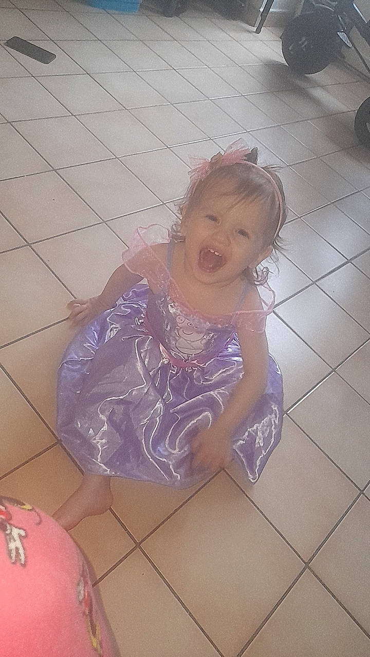 Chelsea participe au concours pour gagner de l'argent avec cette photo : automotive_tire, baby_toddler_clothing, child, dress, floor, flooring, fun, happy, human_leg, leisure, pattern, person, pink, purple, sitting, skin, smile, thigh, tire, toddler