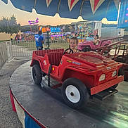 Lilith joined the competition — help win amazing prizes! amusement_park, carnival, child, colorful, evening, fairground, family, happy, jeep, outdoor, playground, plush_toys, portrait, prize_booth, red_vehicle, ride, smiling, steering_wheel, toddler, toy_car