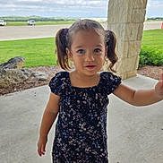Lilith is registered to the contest to win money with this photo: child, girl, pigtails, dress, floral_pattern, porch, concrete_floor, stone_pillar, green_grass, outdoor, daylight, curious_expression, person, young_child, casual_clothing, nature, small_hand, blue_eyes, standing, portrait