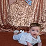 baby, infant, child, blue_eyes, white_clothing, socks, carpet, sequin_backdrop, bunting, decorations, portrait, cute, lying_down, indoor, smiling, face, hands, tummy_time, curious, young