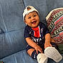 Neithan a rejoint le concours — aidez-le/la à gagner de superbes lots ! baby, child, smiling, sitting, couch, blue_couch, hat, baseball_cap, white_shoes, socks, sportswear, happy, indoor, person, cute, portrait, apparel, footwear, infant, clothing