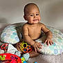 baby, child, smile, toy, pillow, bed, stuffed_animal, sock, indoor, playtime, infant, colorful, happy, cute, nursing_pillow, round_toy, soft_toy, clothing, person, room