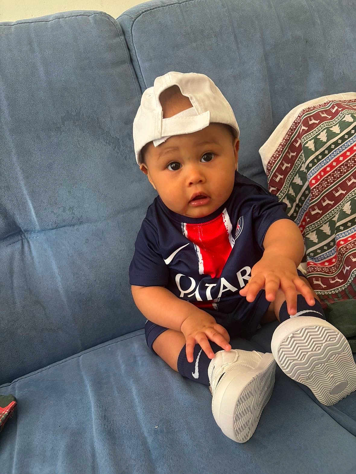 Neithan participe au concours pour gagner de l'argent avec cette photo : baby, child, cap, jersey, sneakers, couch, blue_couch, sitting, curious, wide_eyes, hand, footwear, indoor, clothing, person, portrait, young, sporty, comfortable, home